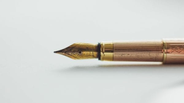 A gold fountain pen lain on its side on a white table.