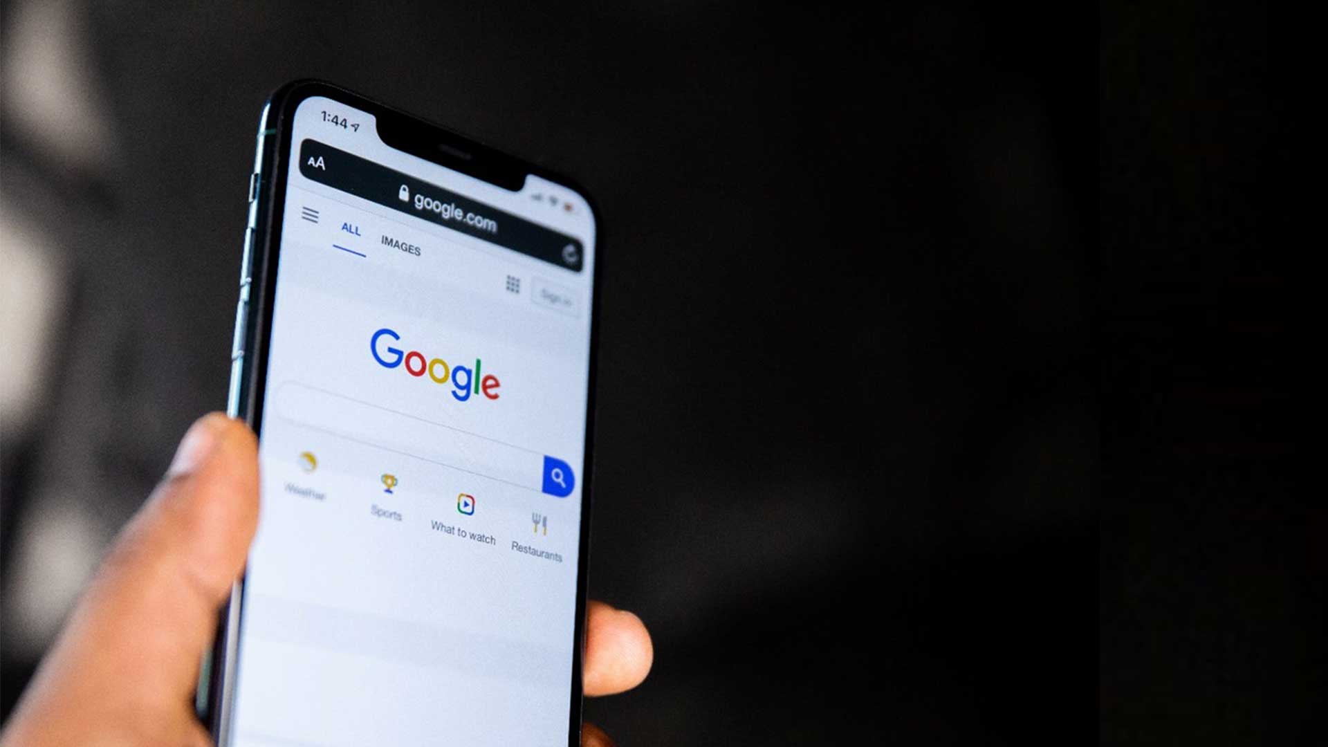A person holding up a phone with the Google homepage on it.